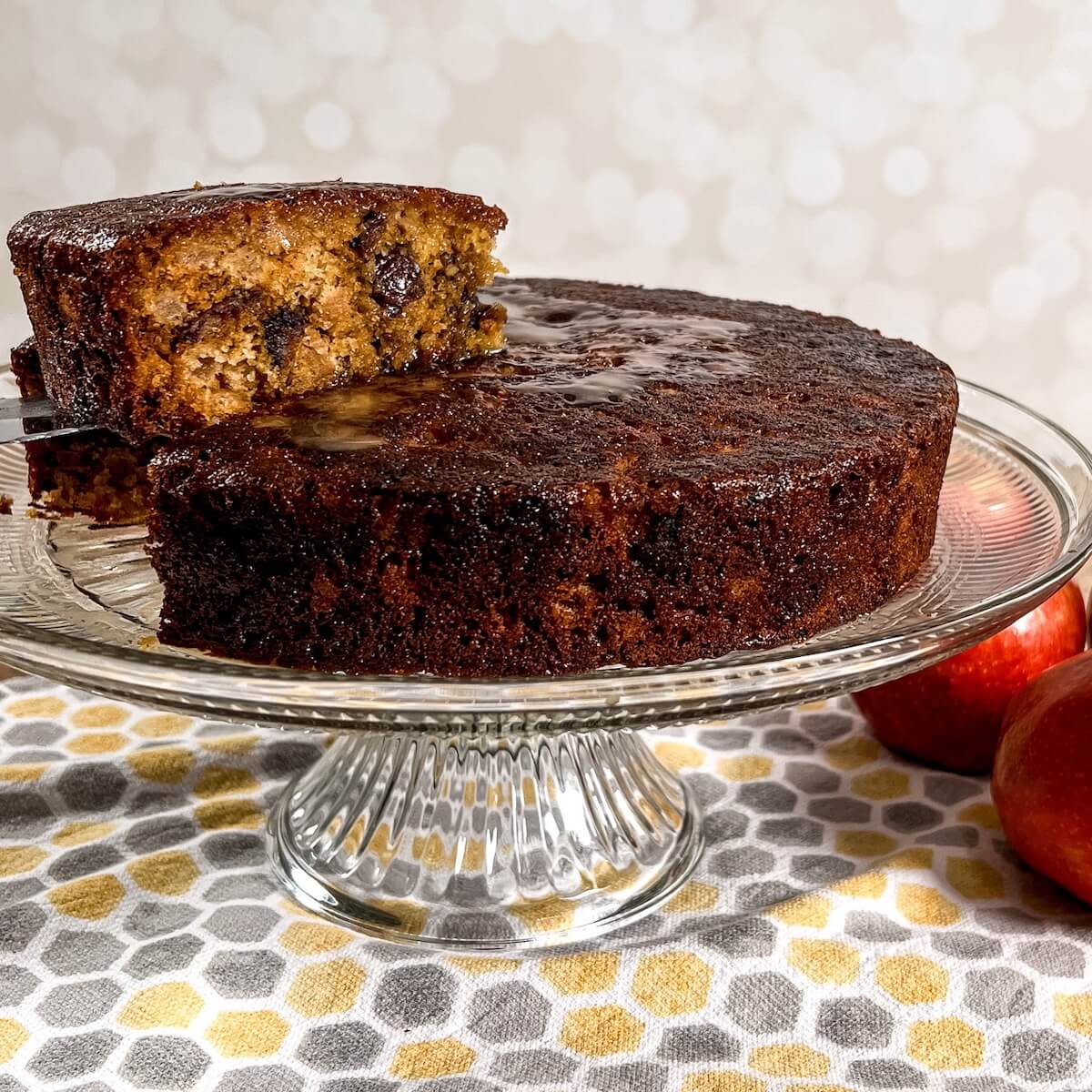 Sticky toffee apple pudding on a cake plate with a cut slice being lifted up.