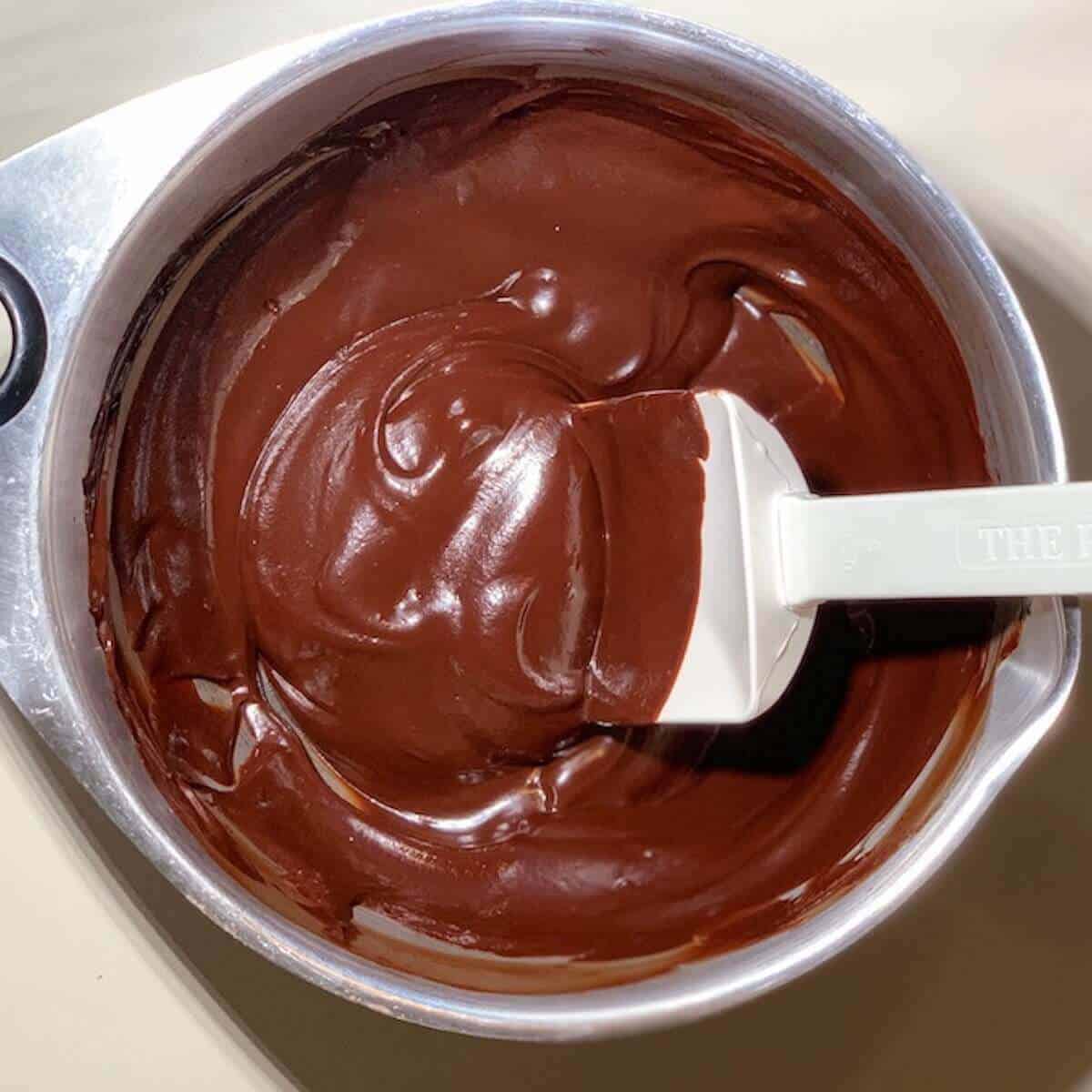Chocolate ganache in a metal bowl with a white spatula.