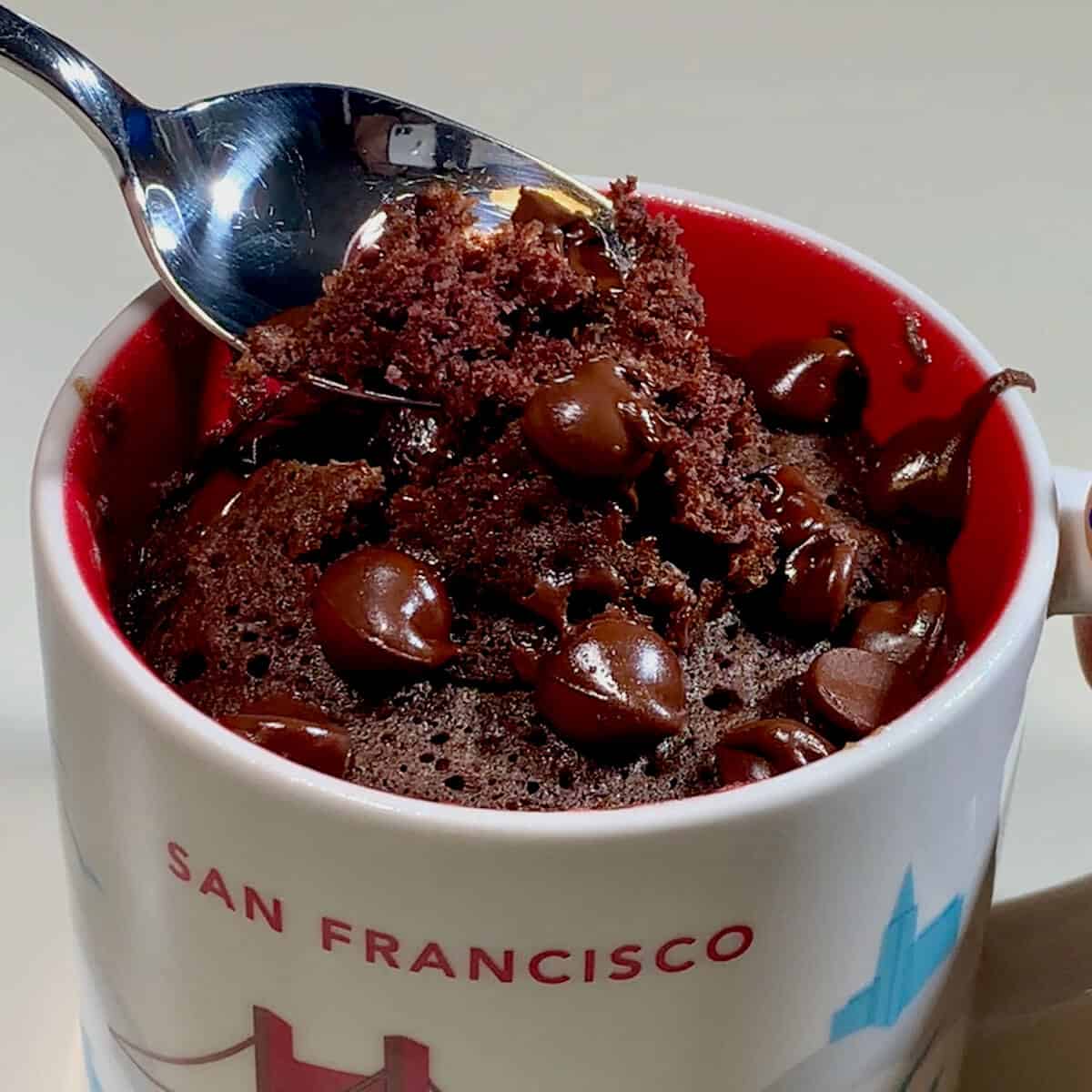 Chocolate mug cake with spoon lifting cake.