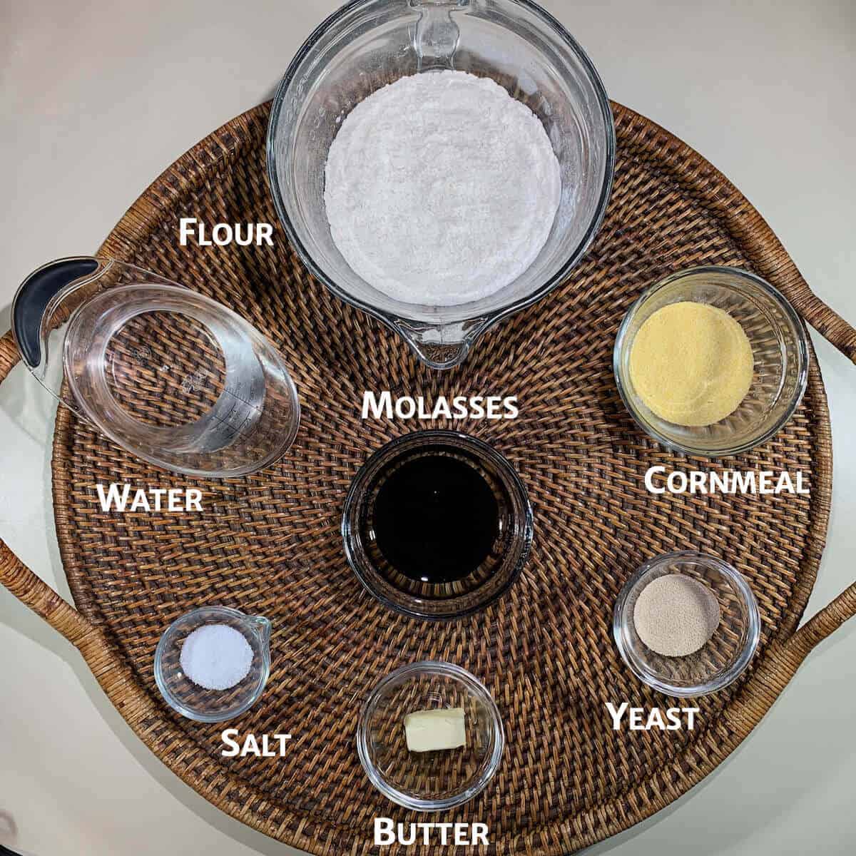 Colonial Bread dough ingredients portioned into glass bowls on a woven tray from overhead.