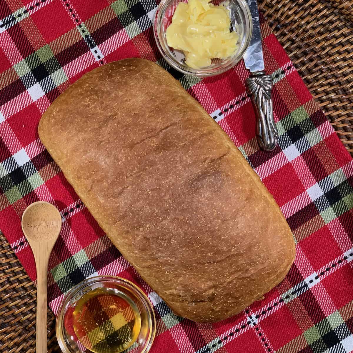 Unsliced Colonial Bread on plaid towel with butter and honey from overhead.