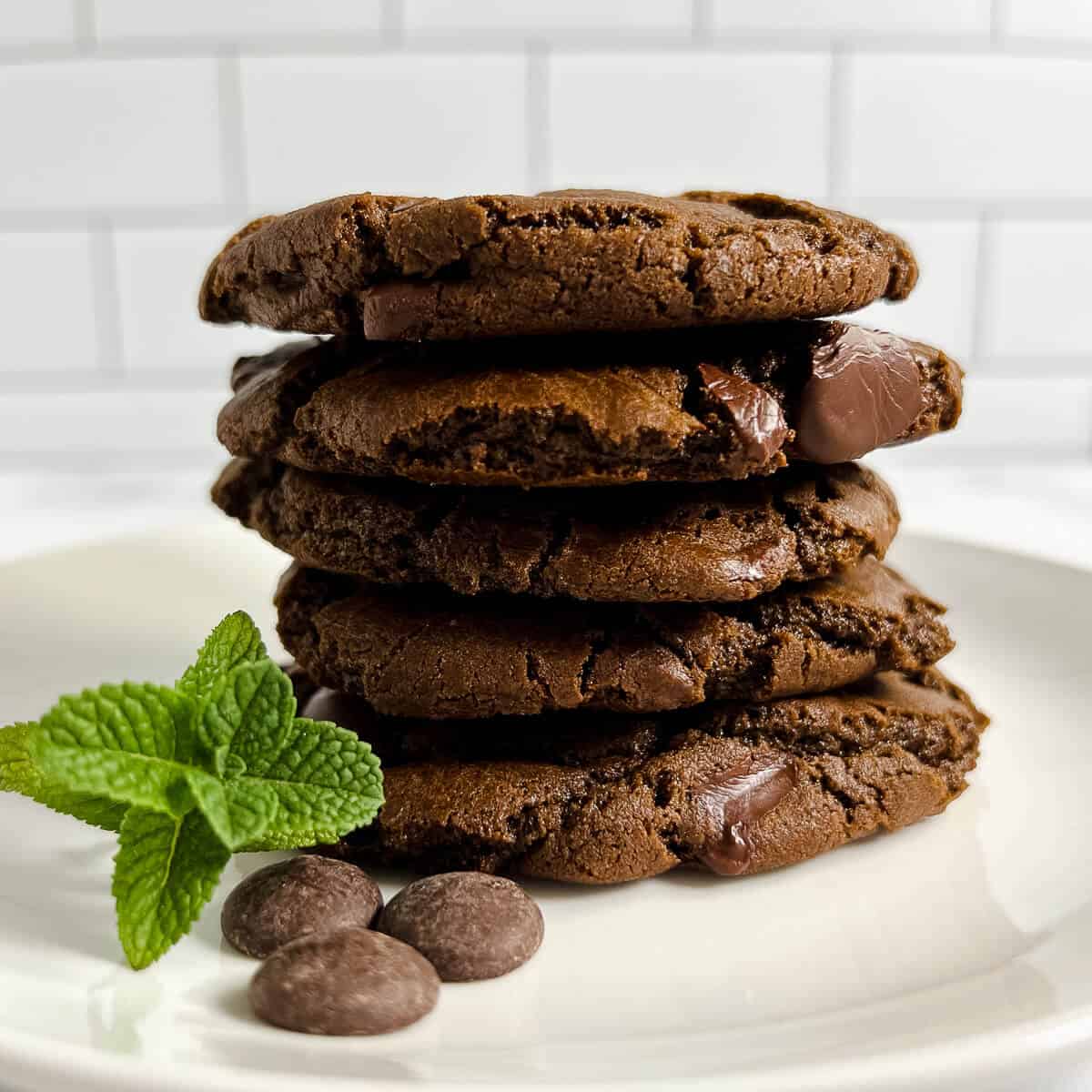 Stack of Double Chocolate Mint Cookies on a white plate with mint and chocolate wafers.