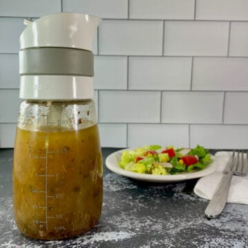 Bottle of herb vinaigrette in foreground and plated salad in background.