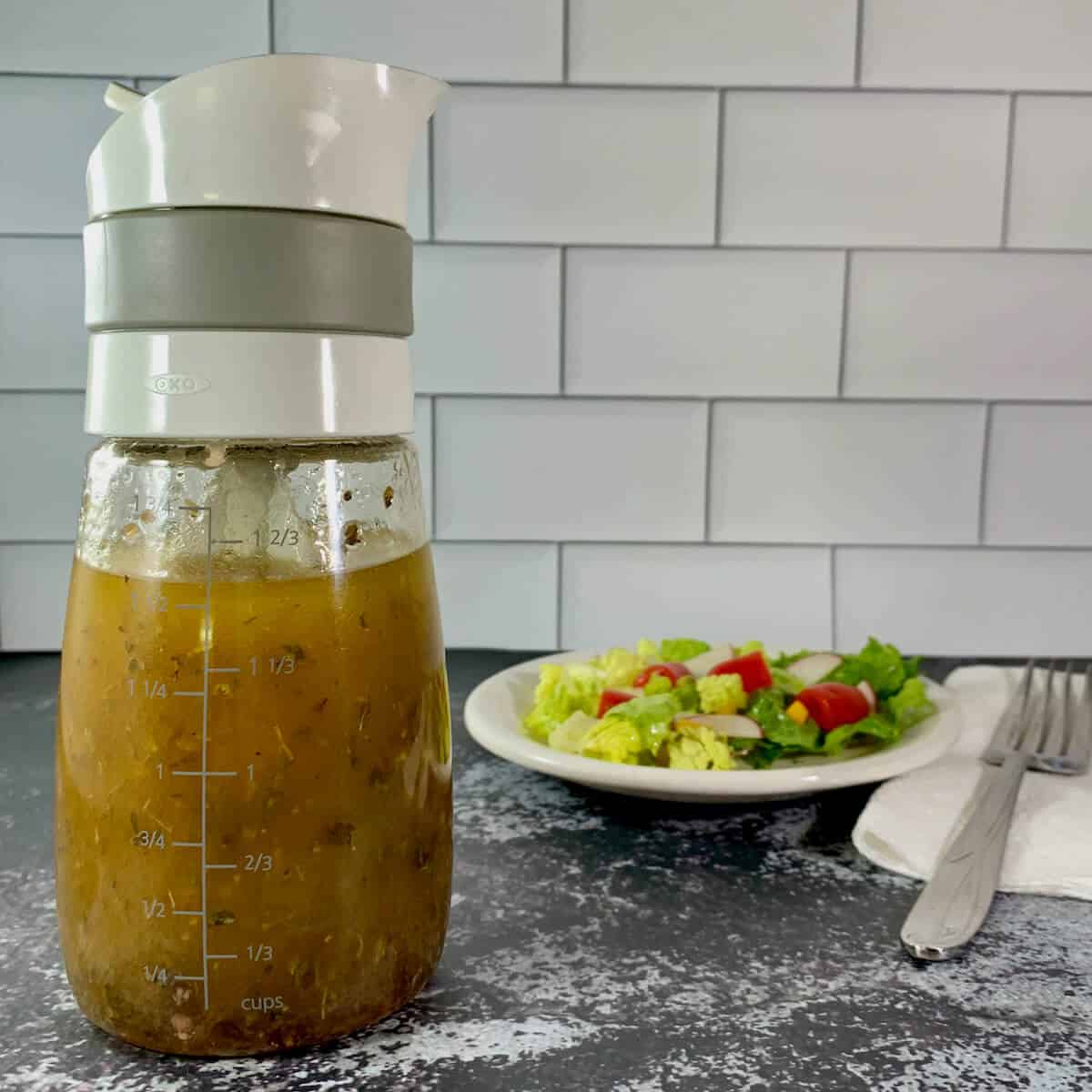 bottle of herb vinaigrette in foreground and salad in background