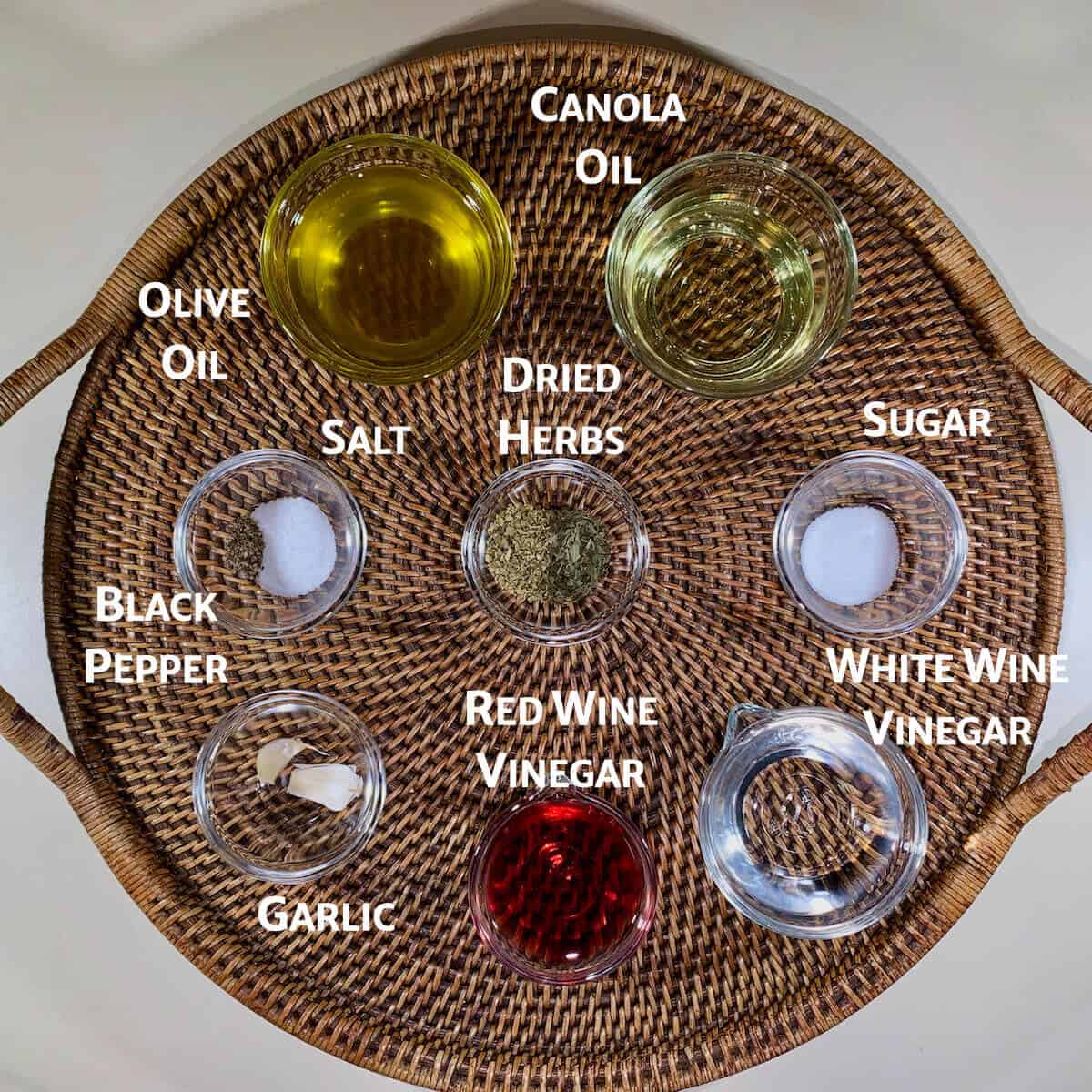 Ingredient for herb vinaigrette portioned in glass bowls on a wooden tray.