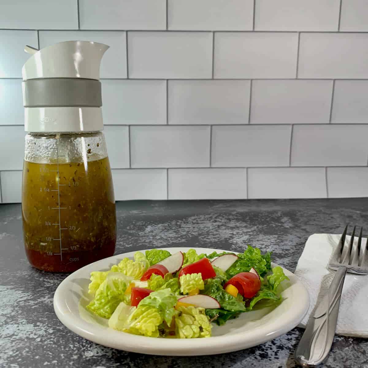 Plated salad with fork in foreground and bottle of herb vinaigrette in background.