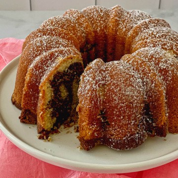 Marble Bundt Cake on a white cake stand with slice removed.