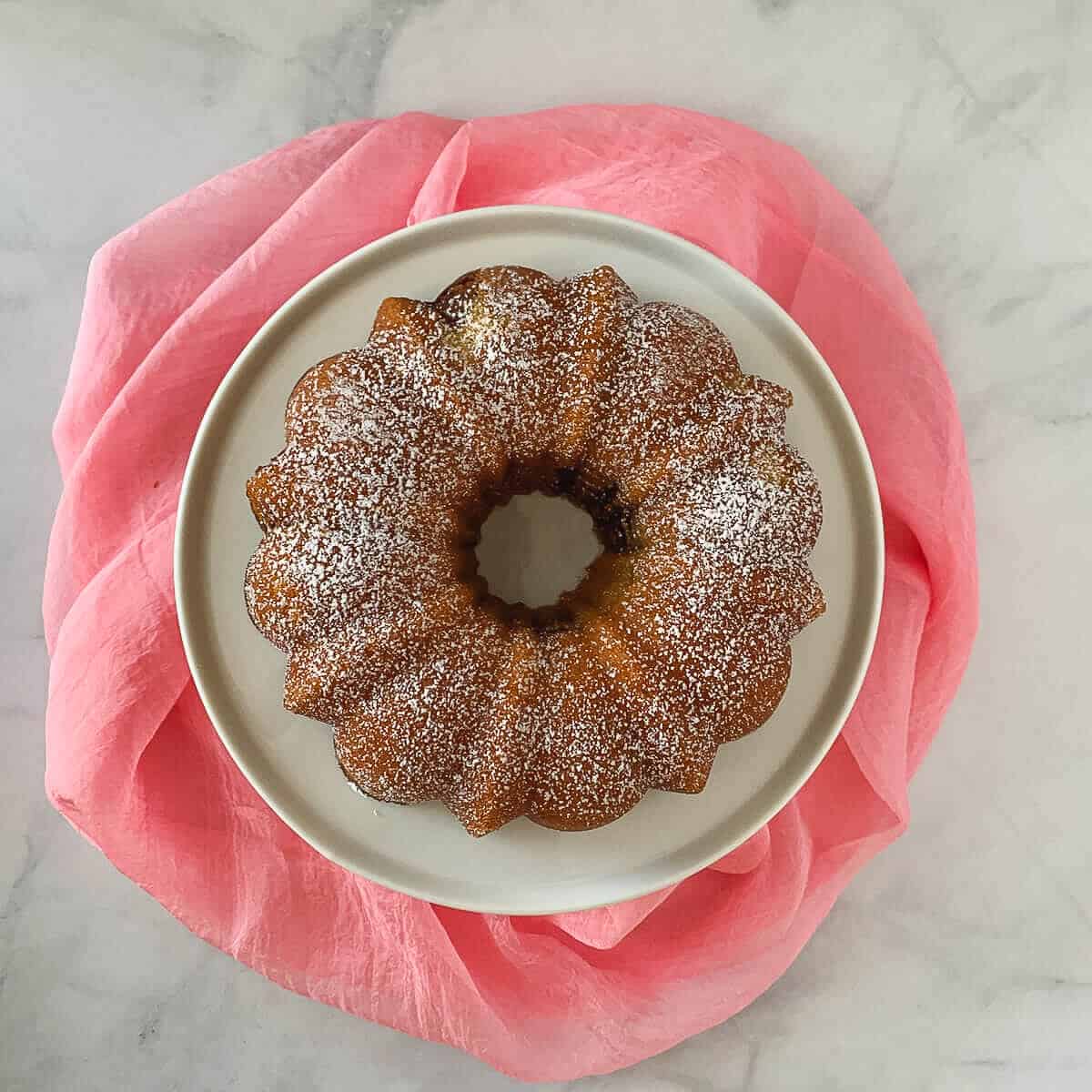 Marble Bundt Cake on a white cake stand with a pink scarf below from overhead.