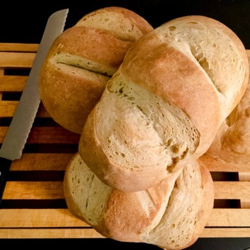 Three stacked sourdough bread loaves on a cutting board next to a bread knife.