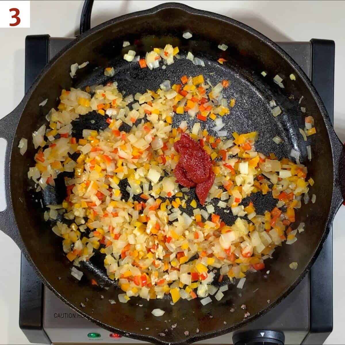 Adding tomato paste to cooked vegetables.