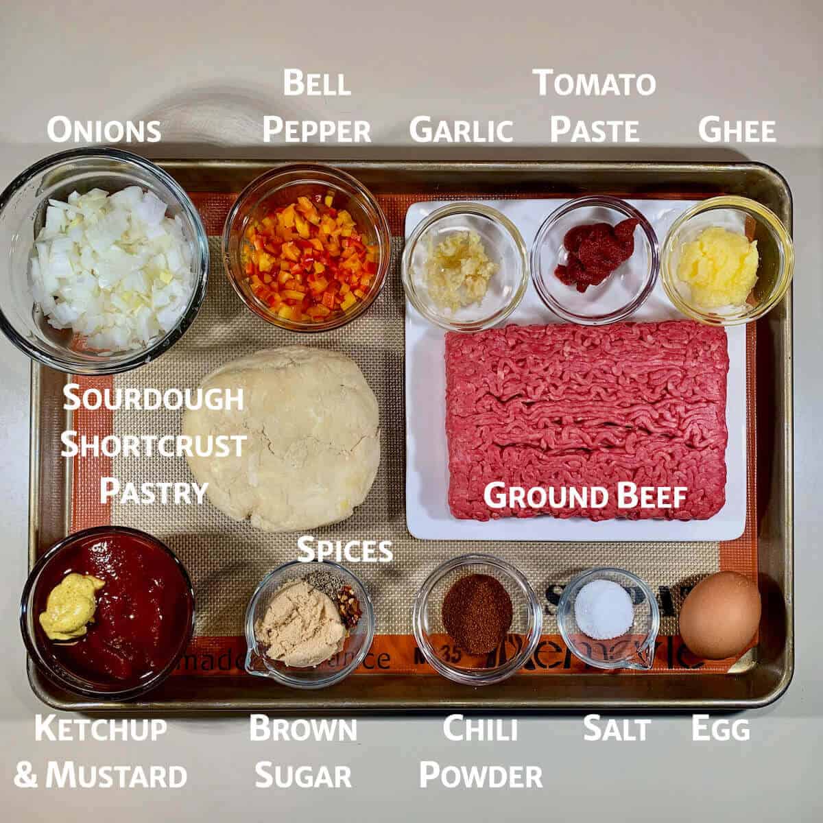 Ingredients for Sloppy Joes pasties portioned into glass bowls on tray from overhead.