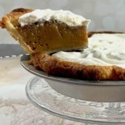 Butterscotch Pie with a sliced lifted on a glass cake stand and flowers below Pinterest banner.