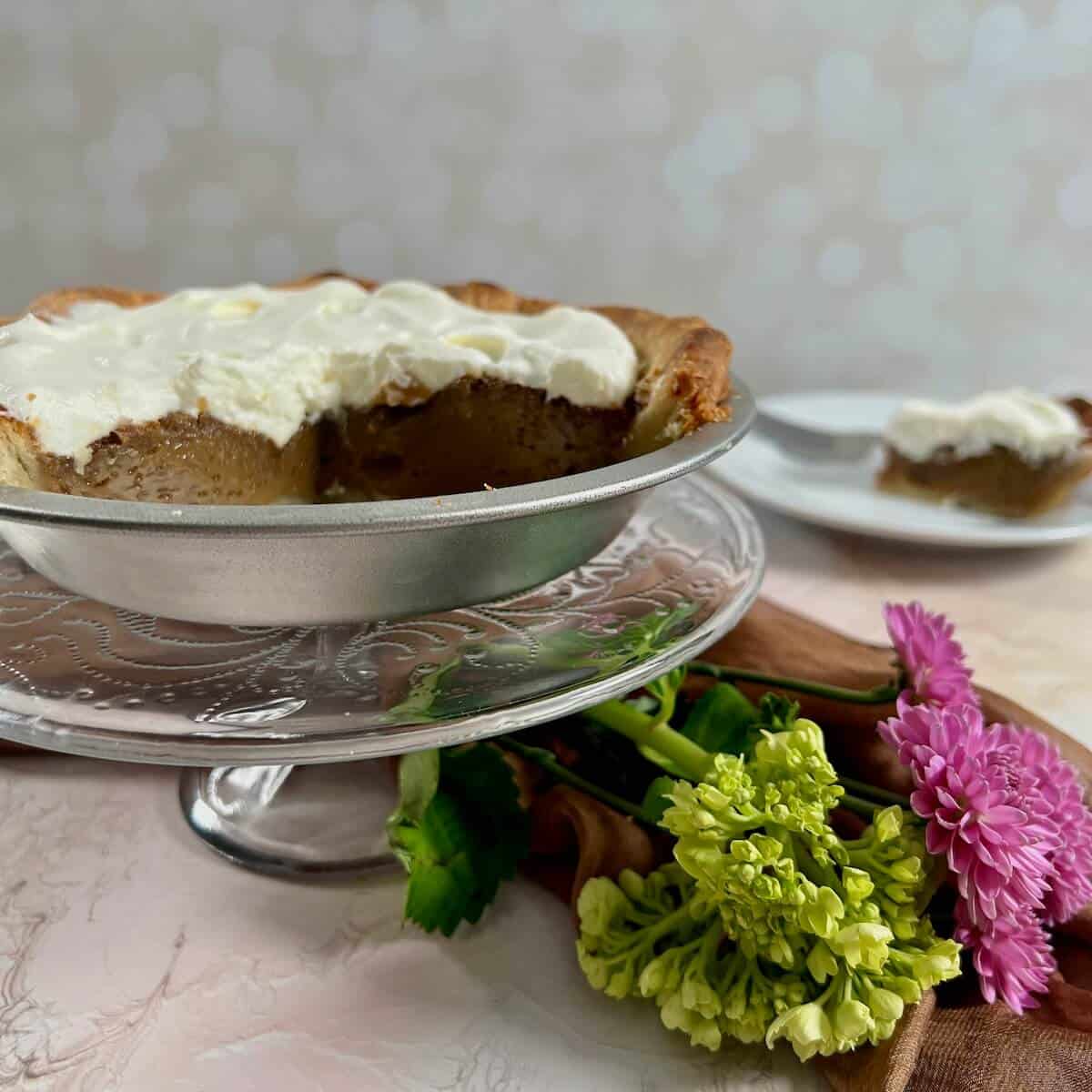 Slice of Butterscotch Pie on a blue and white plate with cut pie and flowers behind.