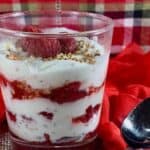 Glass filled with Cranachan layers next to a spoon on a red & plaid scarf Pinterest banner.