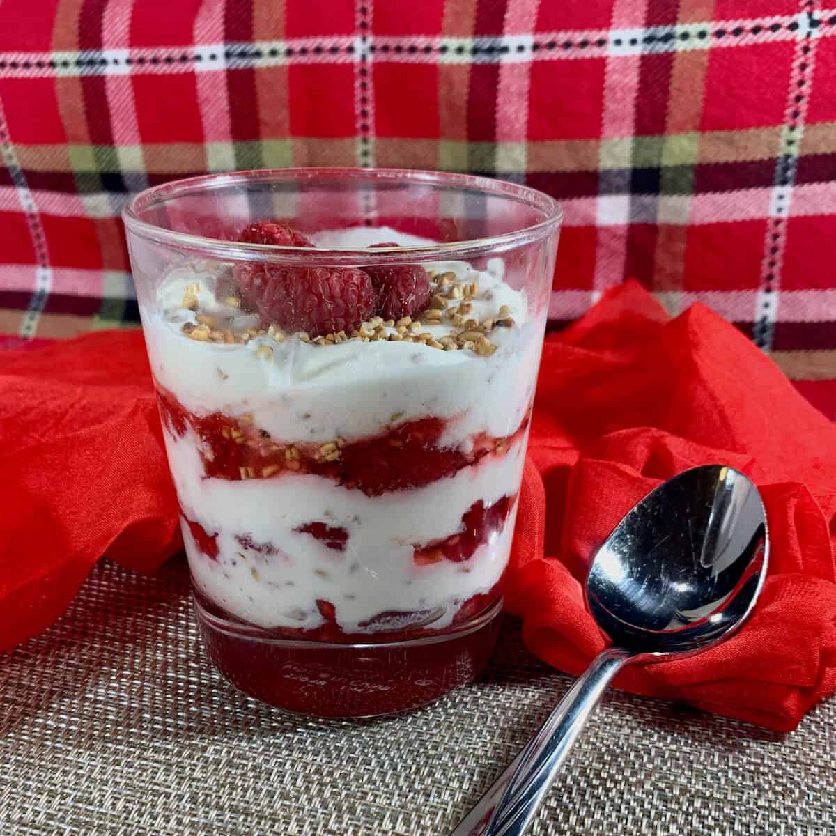 Glass filled with Cranachan layers next to a spoon on a red & plaid scarf.