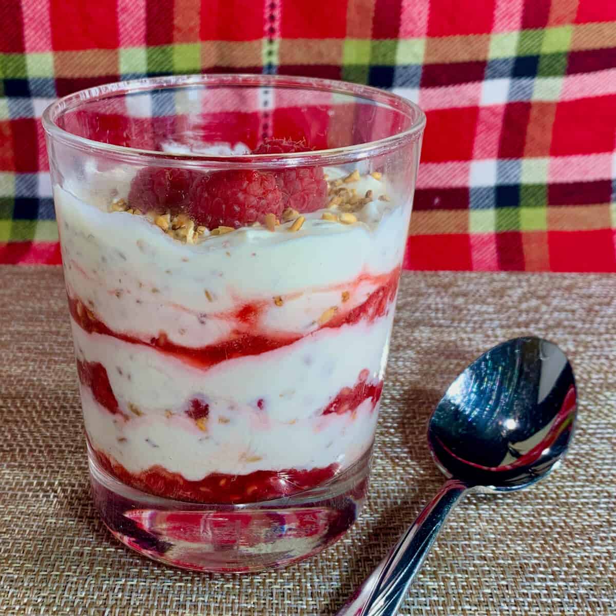 Glass filled with Cranachan layers next to a spoon on a plaid scarf.