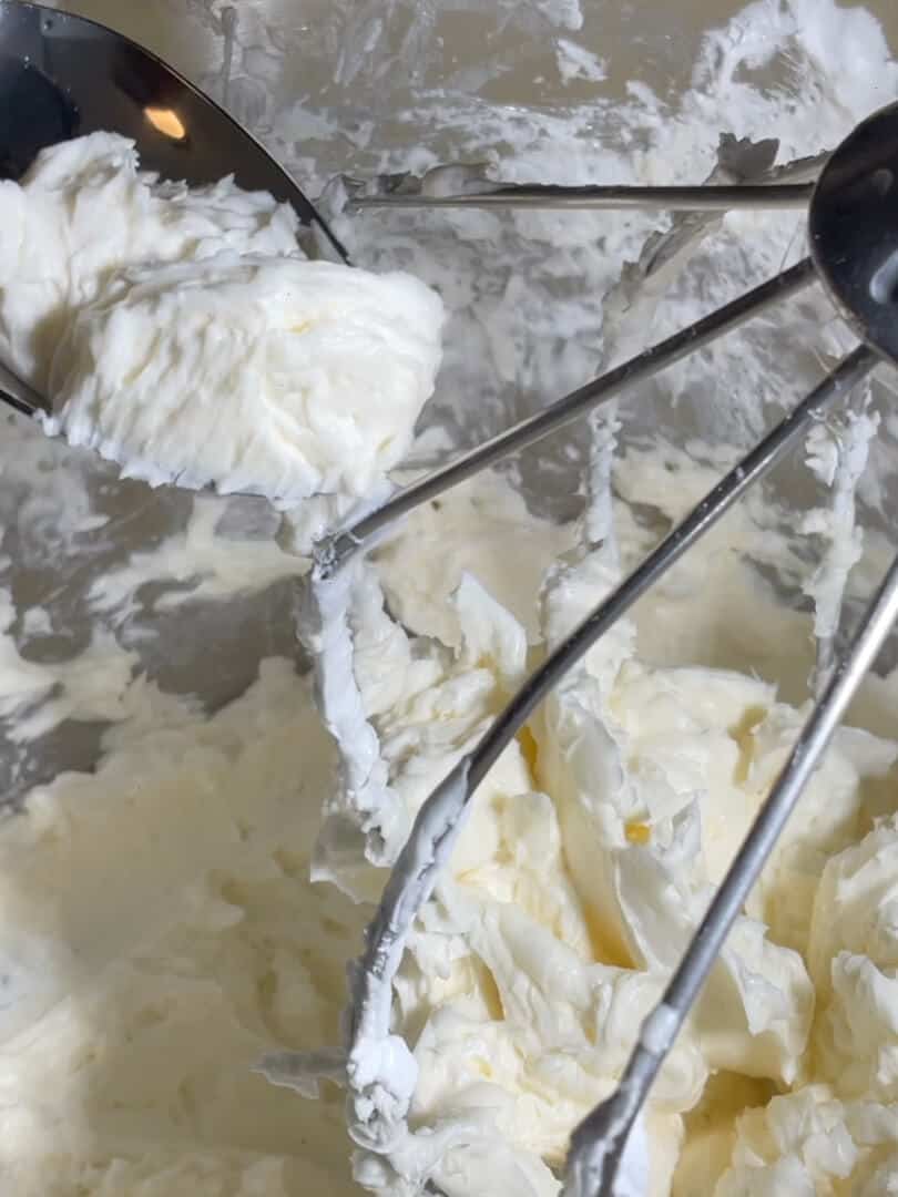 Finished Italian Meringue Buttercream on a spoon above the whisk.