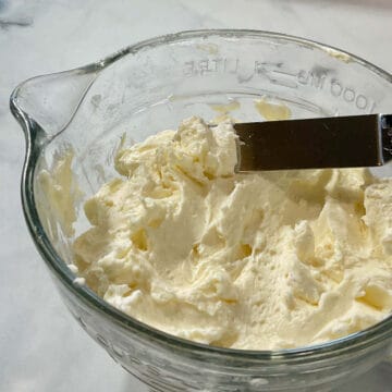 Italian Meringue Buttercream in glass bowl with some lifted on spatula.