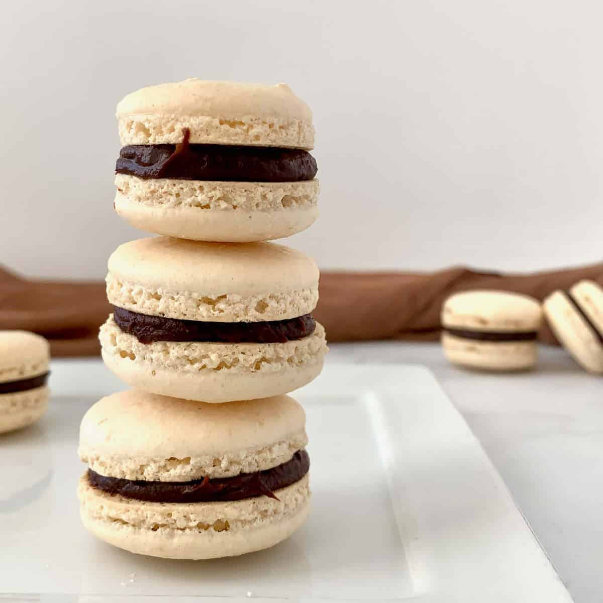 Italian Meringue Macarons stacked on white plate with some in background.