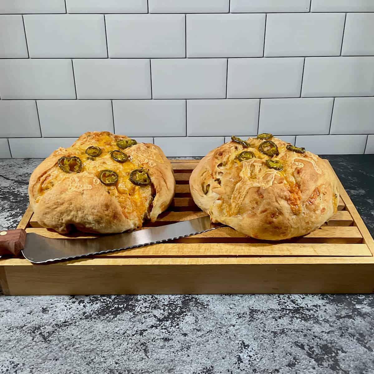 Two loaves of Sourdough Jalapeño Cheddar Bread on cutting board with knife.