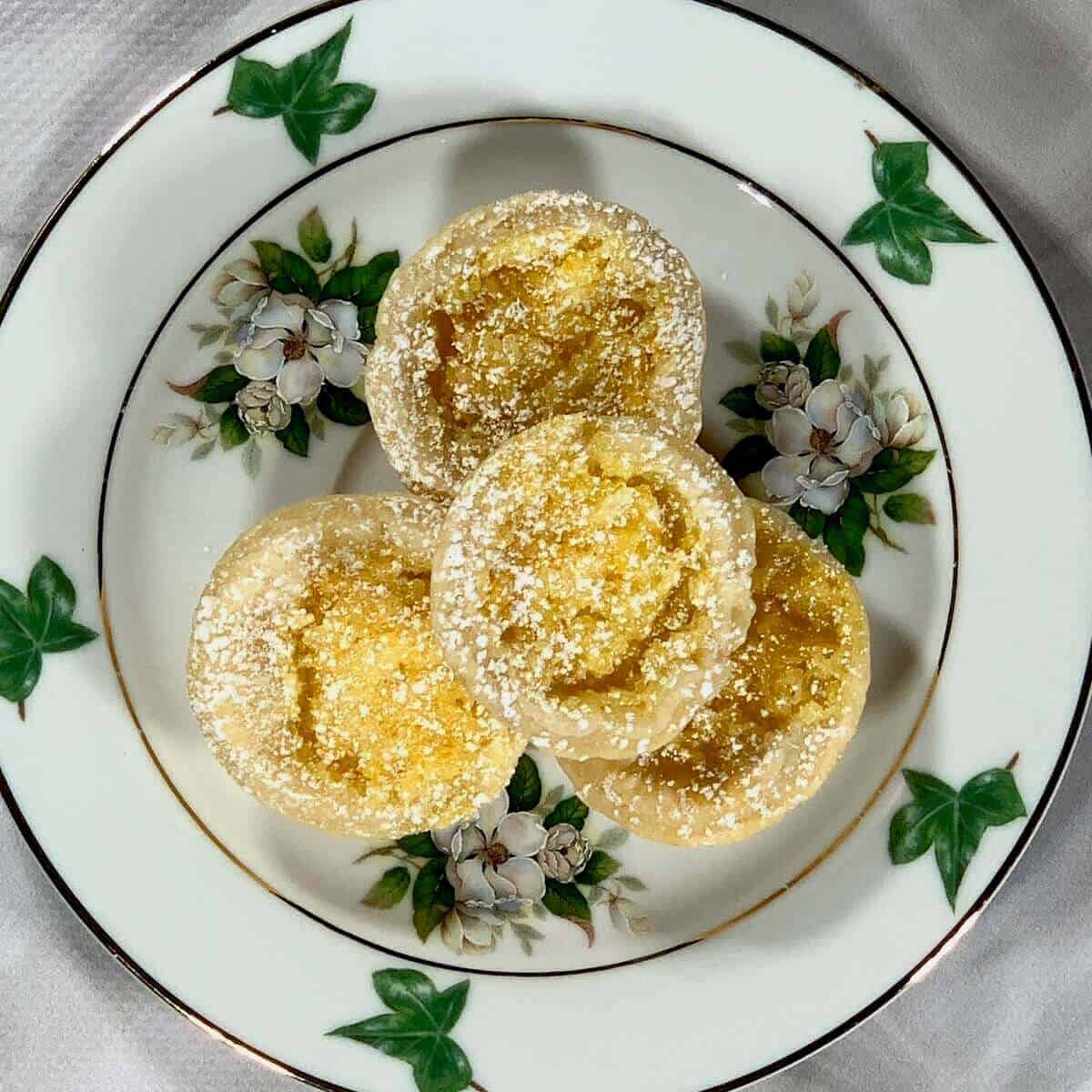 Mini Lemon Tartlets stacked on a white plate with green leaves from overhead.