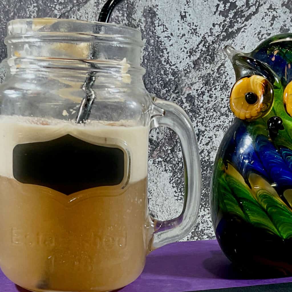 Butterbeer in a mason jar next to a glass owl.