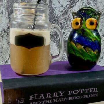 Butterbeer in a mason jar next to a glass owl on a book.