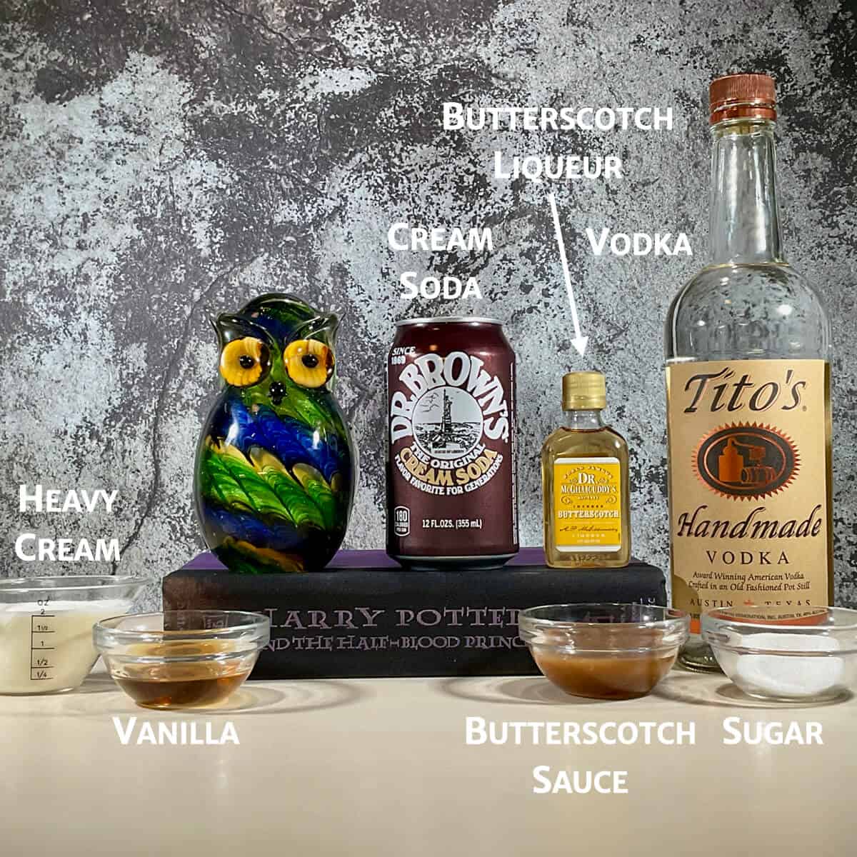Boozy butterbeer ingredients on a counter with a glass owl & book.