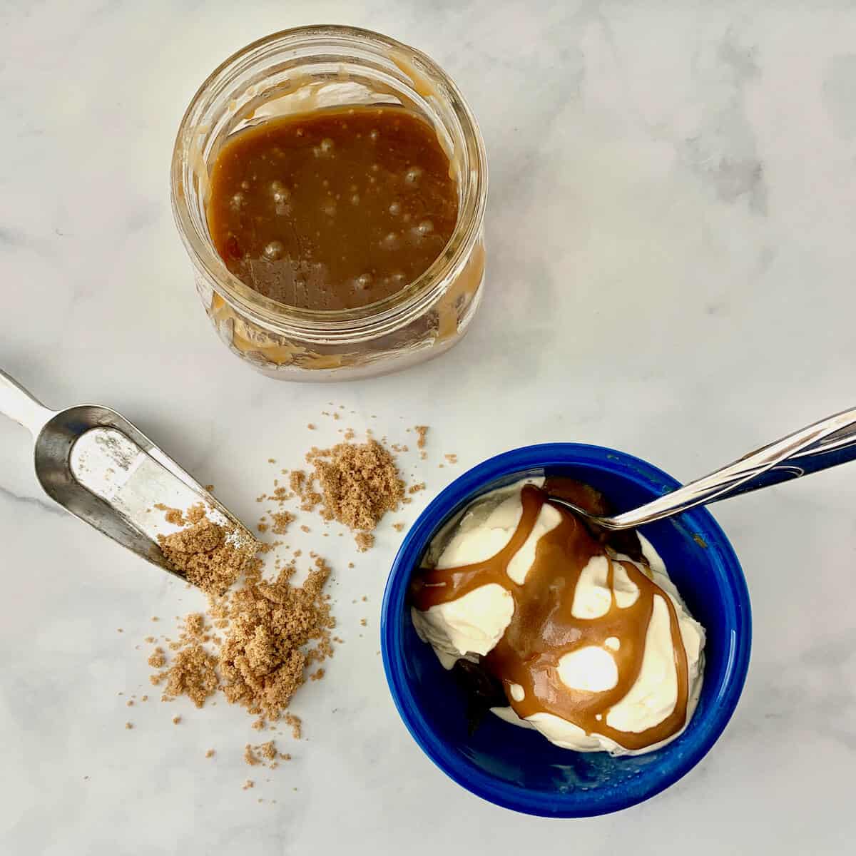 Butterscotch Sauce on vanilla ice cream with jar of sauce & spilled brown sugar from overhead