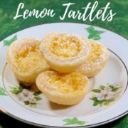 Lemon tartlets stacked on a white plate atop a green background Pinterest banner.