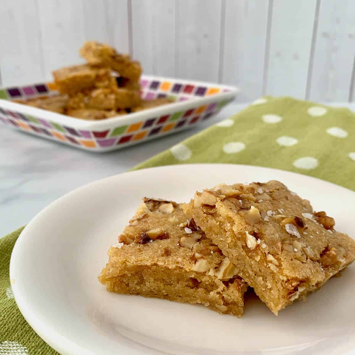 Stack of Maple Walnut Bourbon Blondies on a white plate sitting on a green towel with white polka dots..