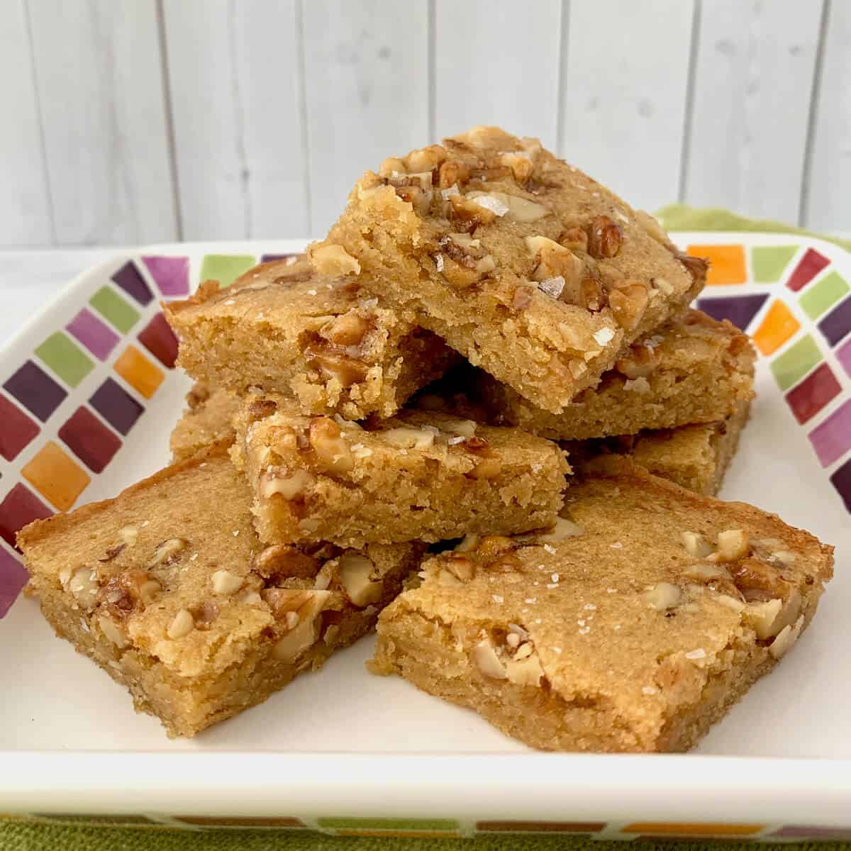 Stack of Maple Walnut Bourbon Blondies on a white plate with multicolored checks.