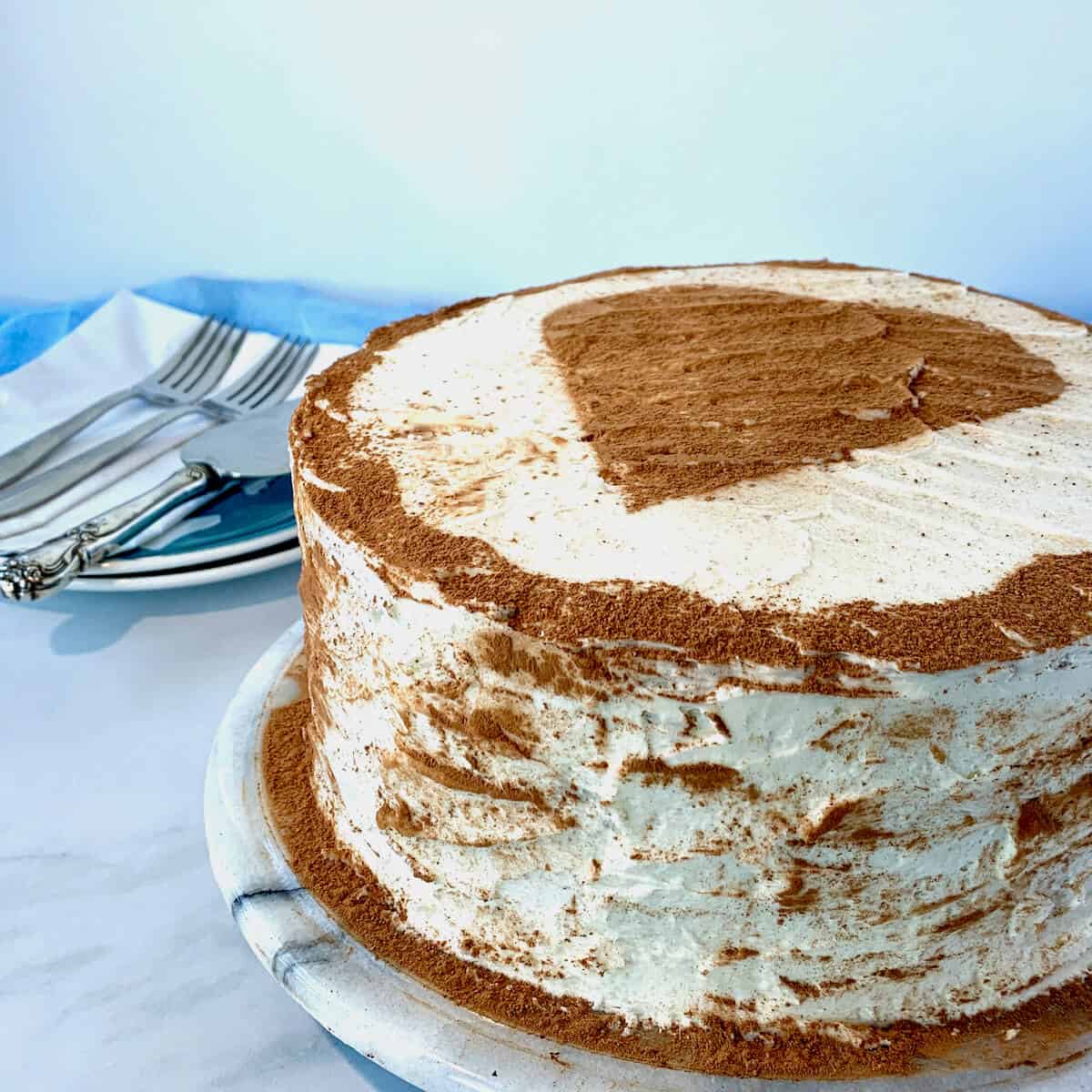 Whole checkerboard cake with heart design on platter with forks & slicer on plate in background.