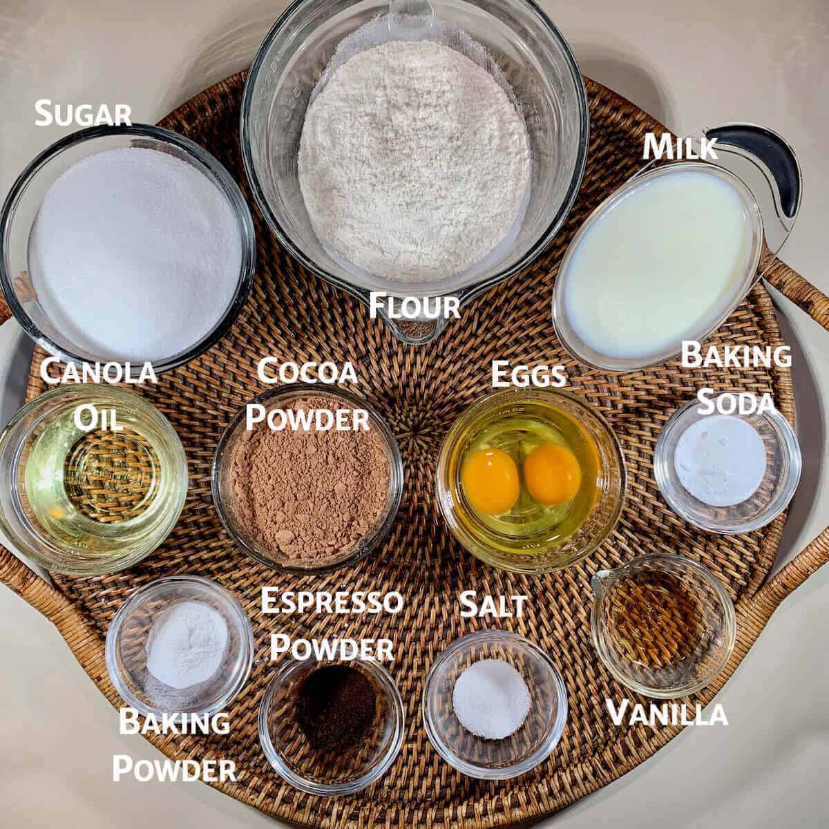 Chocolate cake ingredients portioned into glass bowls on a wooden tray from overhead.
