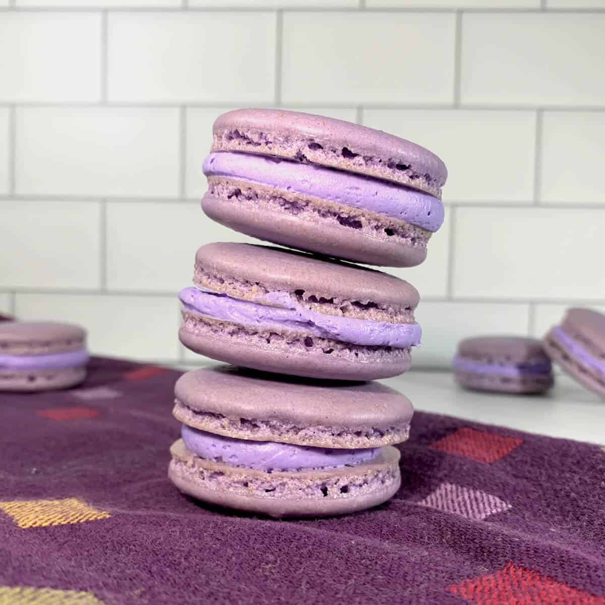 French Macarons with purple buttercream stacked on a purple towel with more in background