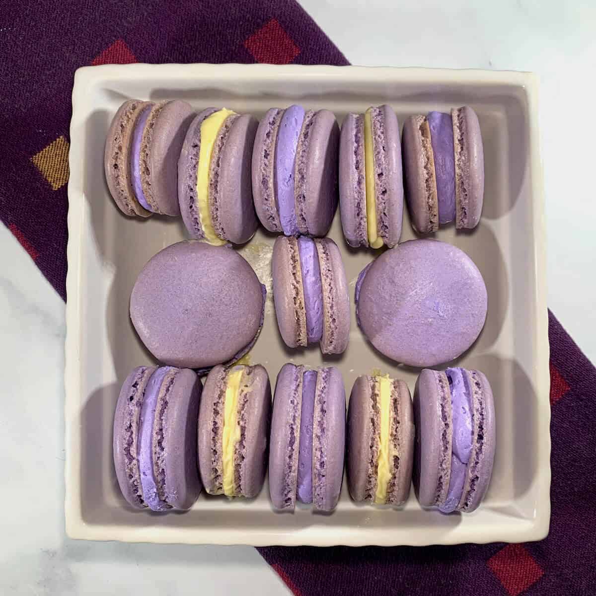French Macarons with purple buttercream & lemon curd laying sideways in a dish on a purple towel from overhead