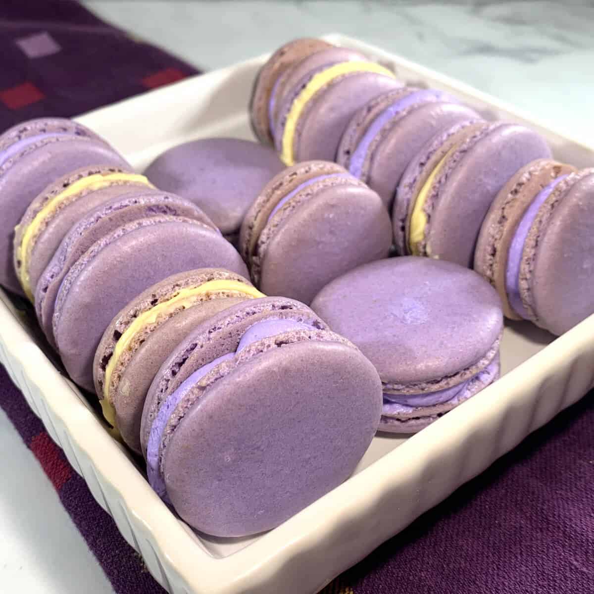 French Macarons with purple buttercream & lemon curd laying sideways in a dish on a purple towel