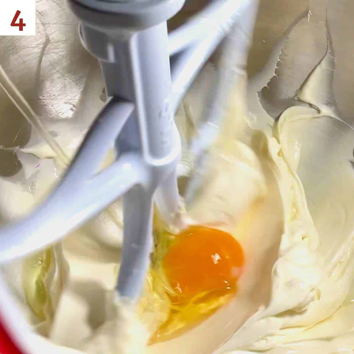 Adding eggs to cheesecake base in the mixer bowl.