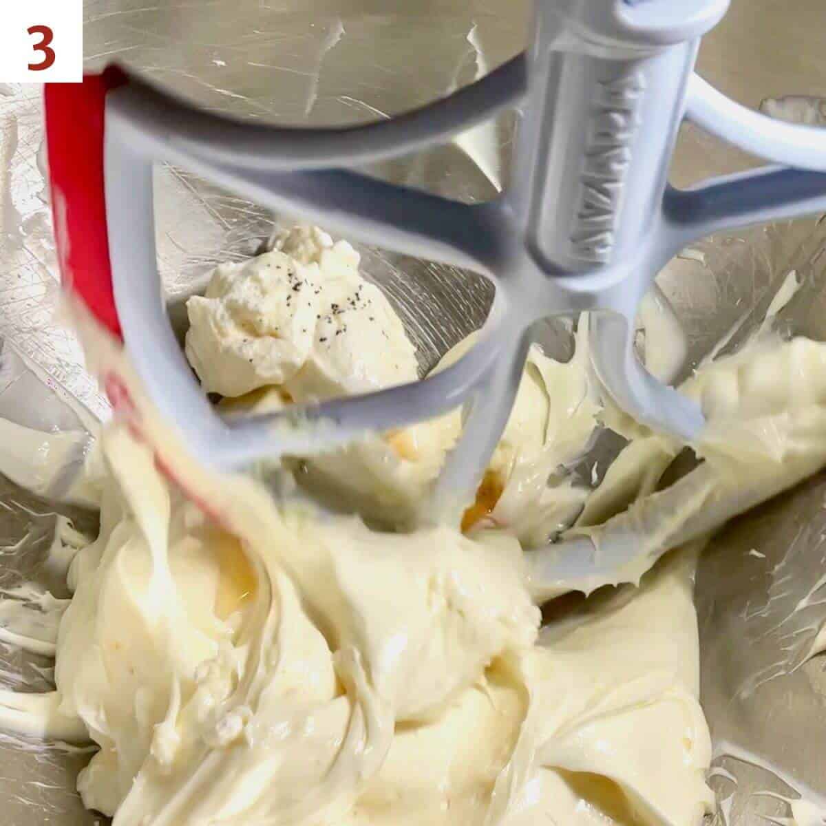 Adding sour cream & vanilla to cheesecake base in the mixer bowl.