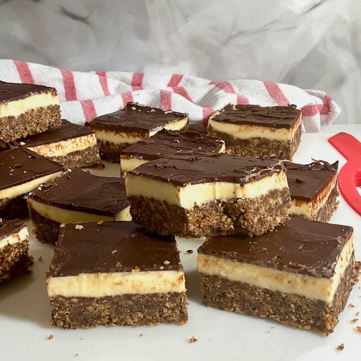 Many Nanaimo Bars and one bitten & stacked on a cutting board.