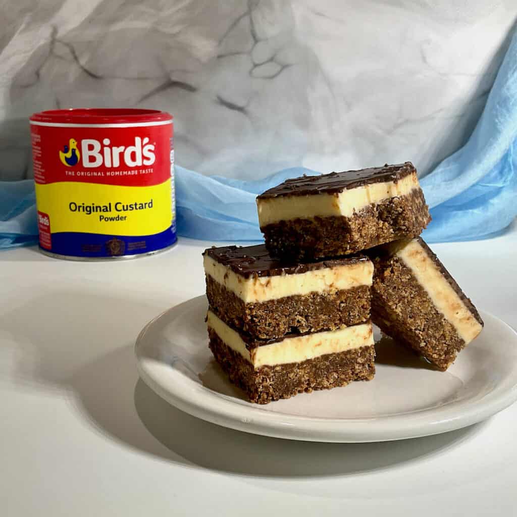 Nanaimo Bars stack and plated with custard powder jar in background.