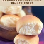 Two sourdough dinner rolls stacked on a purple checked towel with bowl of rolls in background Pinterest banner.