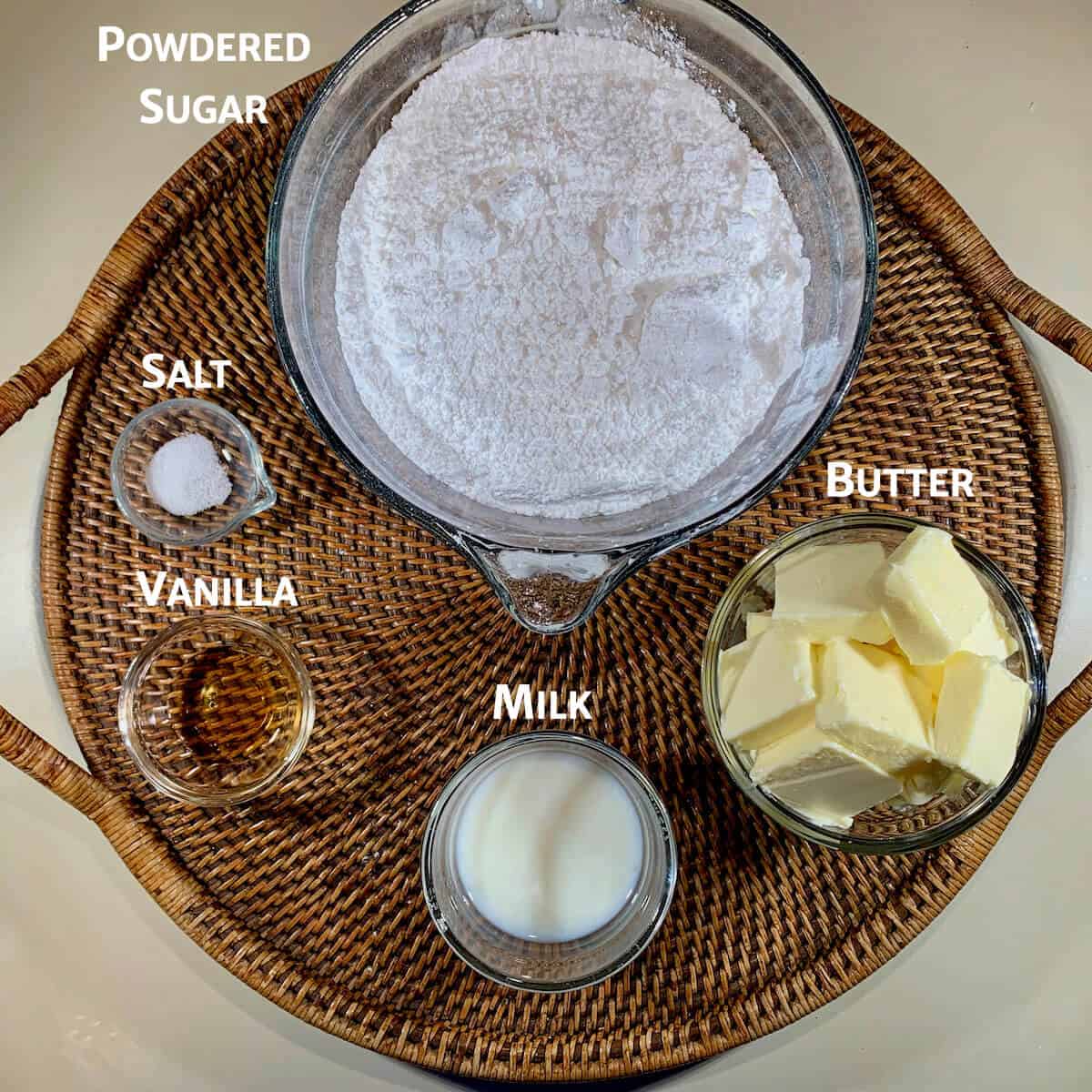 Vanilla buttercream frosting ingredients portioned into glass bowls on a wooden tray from overhead.