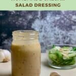 Jar of Caesar salad dressing on a counter with garlic & green salad Pinterest banner.