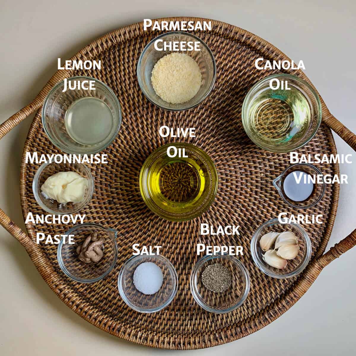 Caesar salad ingredients in glass bowls on a wooden tray.