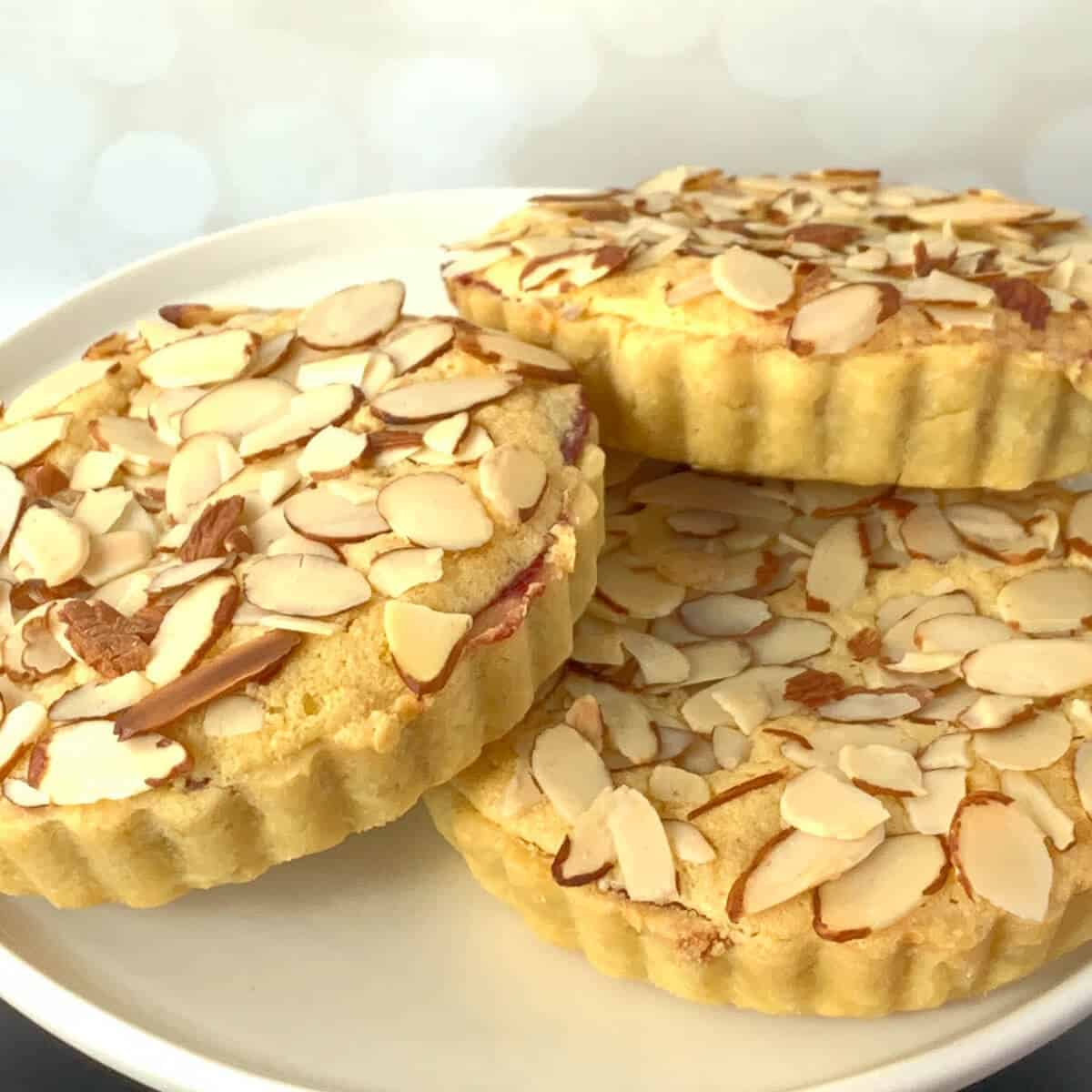 Three mini Bakewell tarts on a white cake stand.