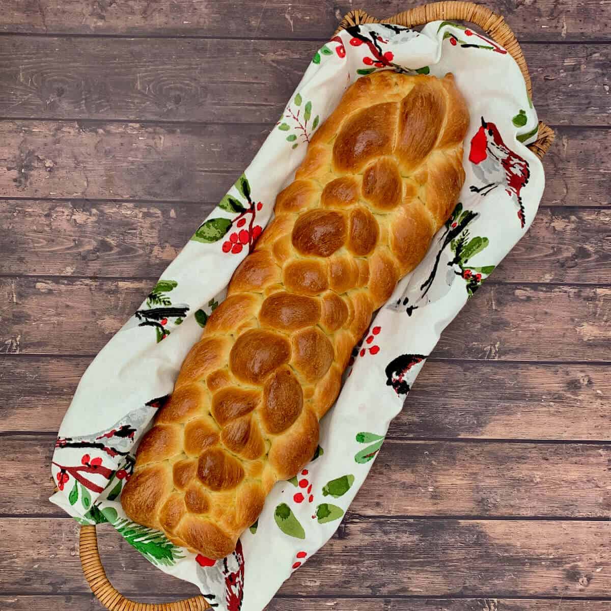 Eight strand braided challah in a napkin lined basket on a wood table from overhead.