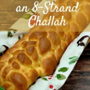 Eight strand braided challah in a napkin lined basket on a wood table Pinterest banner.