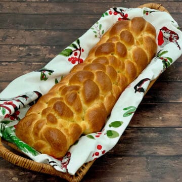 Eight strand braided challah in a napkin lined basket on a wood table.