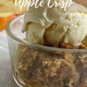 Apple Crisp in a glass bowl topped with vanilla ice cream with apple halves behind Pinterest banner.
